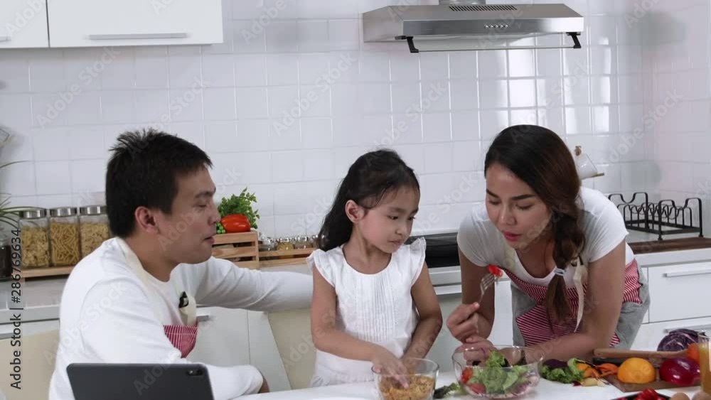 Happy Asian family make a cooking. Father, Mother and Daughter are eating salad, vegetable in the kitchen at home. Healthy food concept and happy holidays