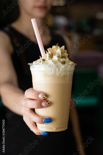 Woman is holding latte with whipped cream, toppings and straw on the outstretched hand photo