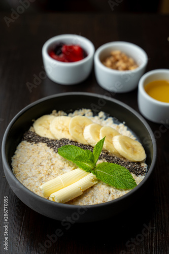 Close up of whole grain porridge with different toppings, served on dark table as a healthy substantial breakfast