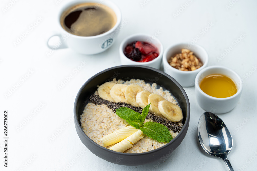 Healthy sweet breakfast with whole grain porridge, chia seeds, butter, banana and other toppings, served with a cup of black coffee on a white background Healthy sweet breakfast with whole grain porridge, chia seeds, butter, banana and other toppings, served with a cup of black coffee on a white background