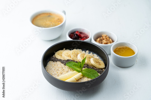 Healthy sweet breakfast with whole grain porridge, chia seeds, butter, banana and other toppings, served with a cup of black coffee on a white background