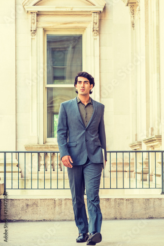 Young Mix Race American Businessman working in New York City, wearing dark blue suit, green undershirt, black leather shoes, carrying laptop computer, walking inside office building, going to work.. © Alexander Image