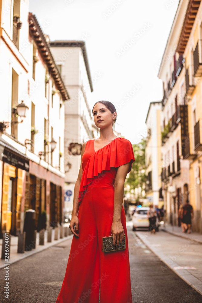 Beautiful brunette young woman with topknot hairstyle wearing red ruffles dress and golden handbag walking on the street. Fashion photo. Beautiful brunette young woman with topknot hairstyle wearing red ruffles dress and golden handbag walking on the street. Fashion photo.