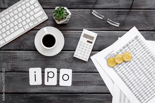 IPO with coins, calculation table, keyboard, coffee on office desk gray wooden background top view