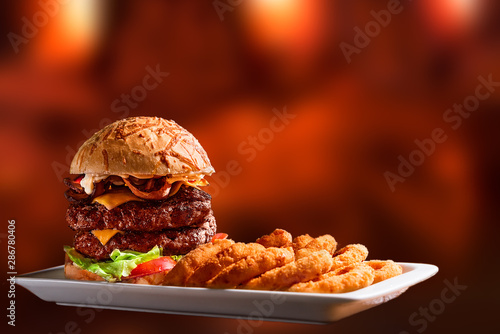 Hamburger double burger cheese bacon tomato lettuce onion rings, isolated on an out of focus wooden fire background