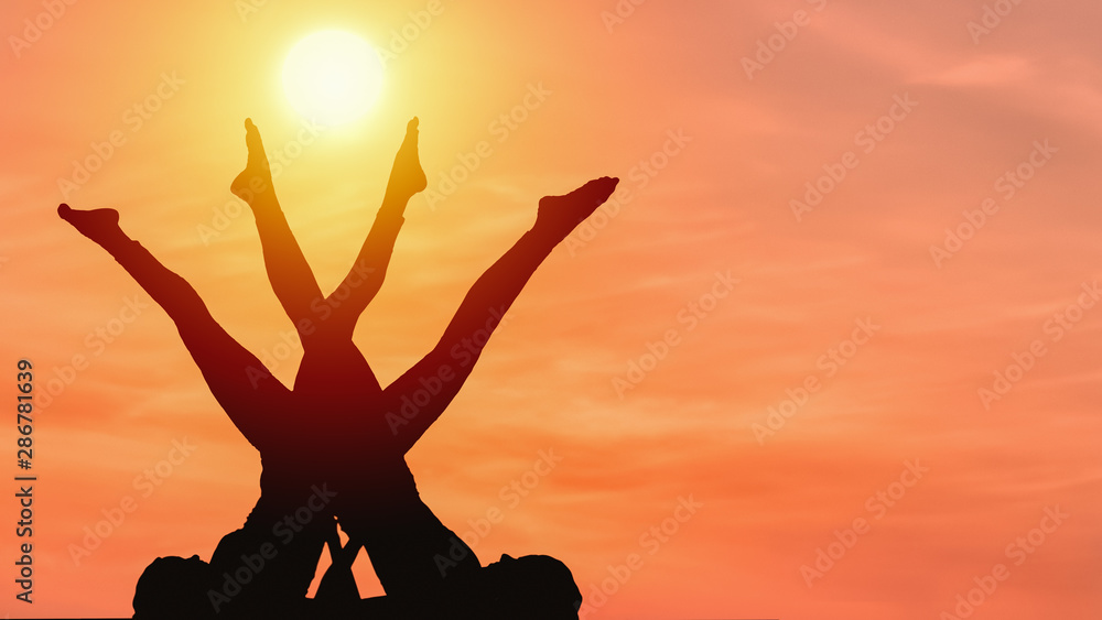 silhouette of two caucasian female posing yoga style with background of sunrising sky