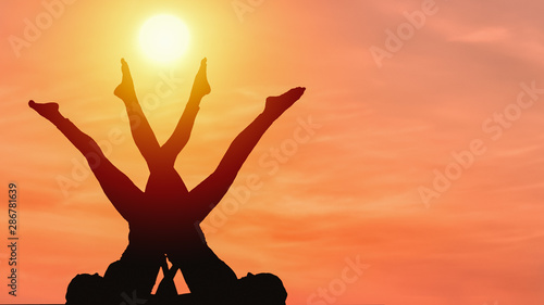 silhouette of two caucasian female posing yoga style with background of sunrising sky photo