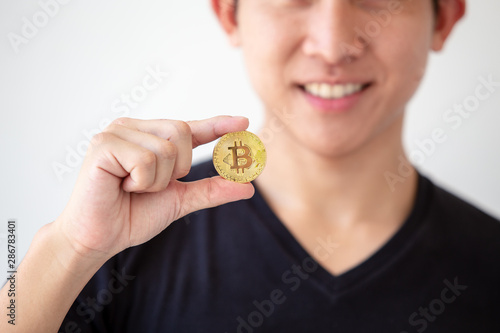 Young asian man hold golden bitcoin coins in hand. Virtual currency. Crypto currency. New virtual money.