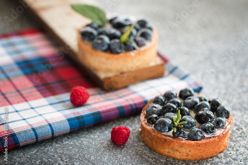 Tartlets with blueberries on the gray table with a checkered napkin, with fresh berries of raspberry. Top view