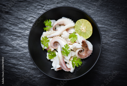 squid salad bowl with lime herbs and spices on black background top view - Tentacles octopus cooked appetizer food seafood cooked in the restaurant