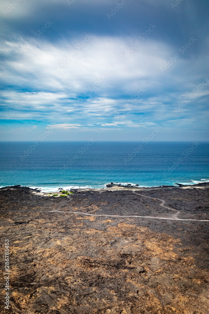 Rough volcanic rock leads to calm deep blue ocean and idyllic clouds