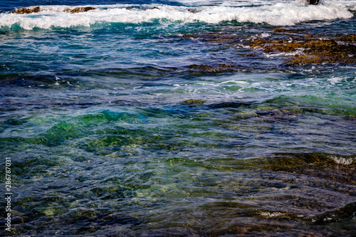Close up of calm ocean waves over deep dark rocks and cool green water in Hawaii