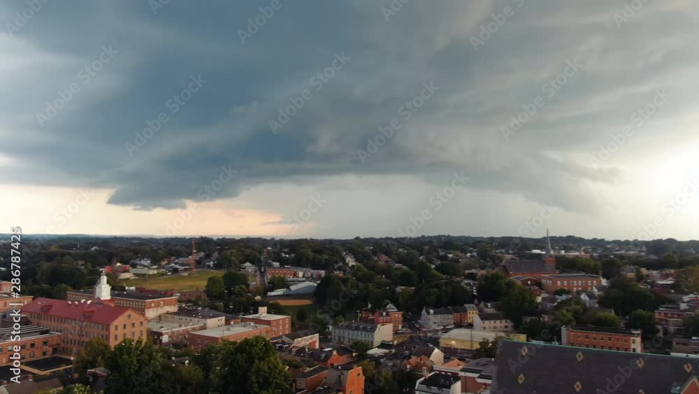 Aerial turn revealing massive storm clouds and summer thunderstorm rolling in above urban city setting
