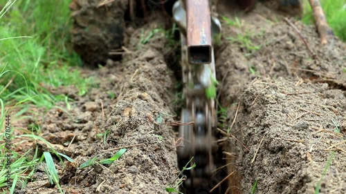 Slow motion, close up view of machine digging a trench for backyard irrigation system. Landscape design and trenching for pipe, conduit or utilities. Large chain spinning to dig a channel in dirt.
