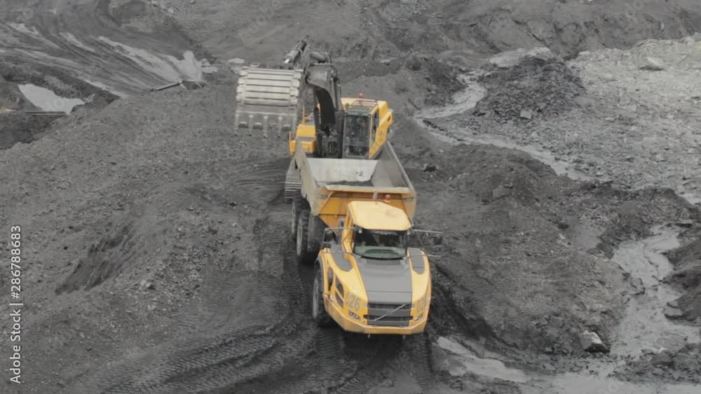 An excavator digs coal and pours it into a yellow dump truck. Open pit coal mining An excavator digs coal and pours it into a yellow dump truck. Open pit coal mining