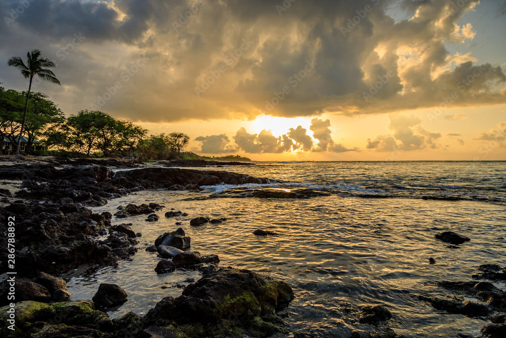 Dark rocks and green trees frame a dramatic sunset in Hawaii