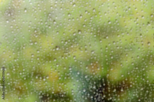 Blurred water drop on glass with ring bokeh and green nature background.