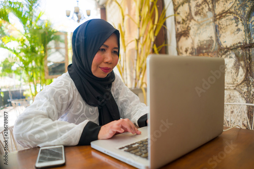  middle age Asian Indonesian Muslim woman in traditional hijab head scarf working relaxed at home garden running online business in internet job success