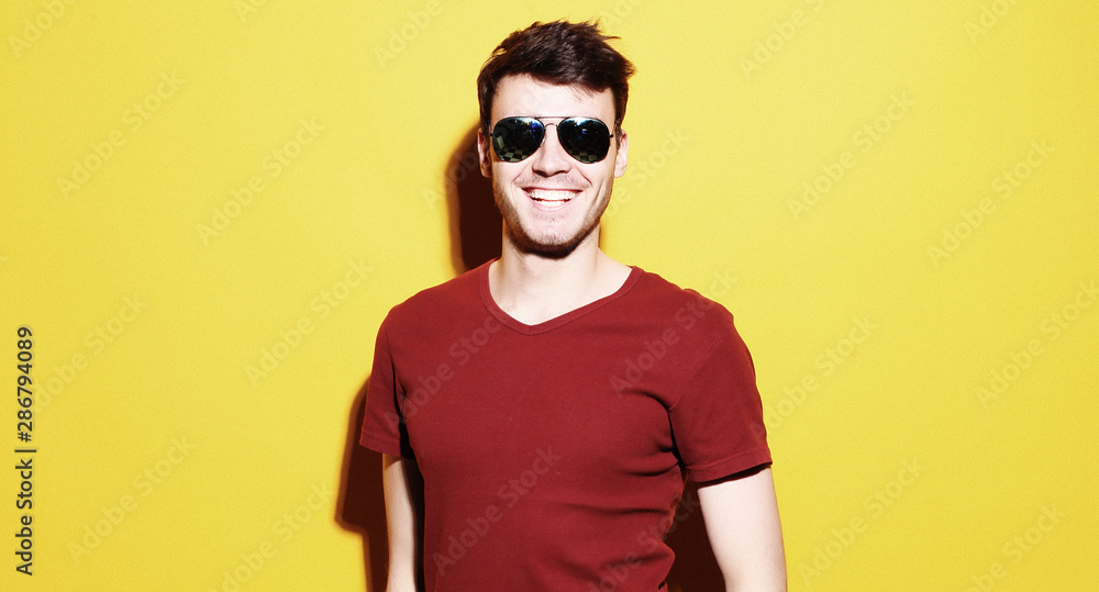 portrait of a young man wearing sunglasses on yellow background portrait of a young man wearing sunglasses on yellow background