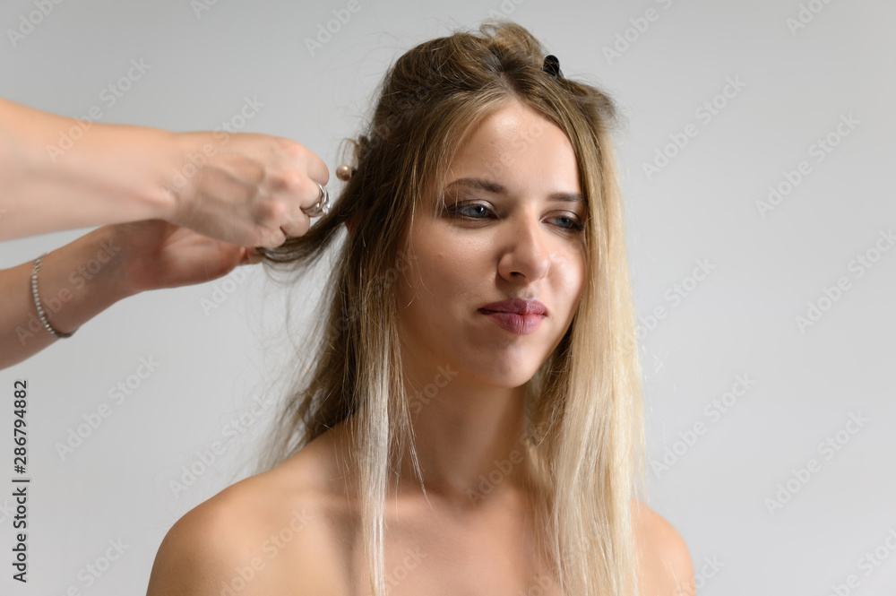 Fototapeta premium A photo of a hairdresser working on a model's hair in a studio. Makes a hairstyle, styling hair on a white background.