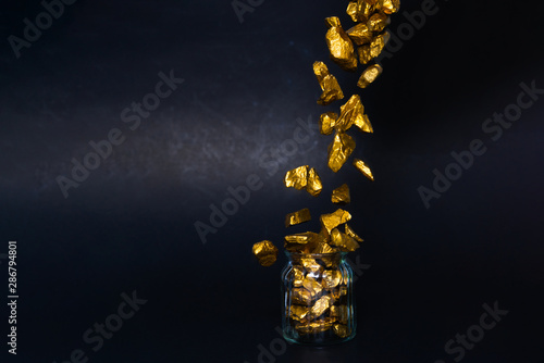Foto Falling gold nuggets or gold ore and glass jar in dark room