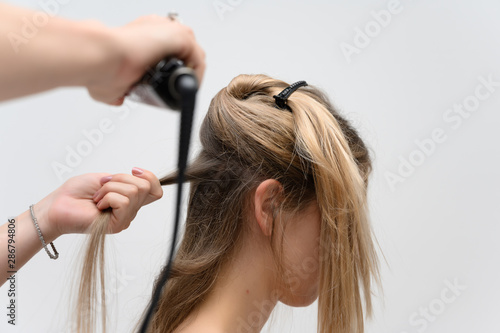 A photo of a hairdresser working on a model's hair in a studio. Makes a hairstyle, styling hair on a white background.
