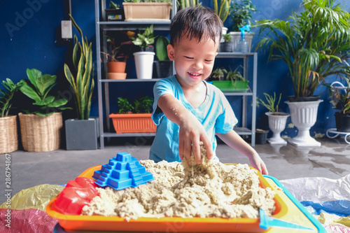 Foto Cute smiling Asian 3 - 4 years old toddler boy playing with kinetic sand in sand