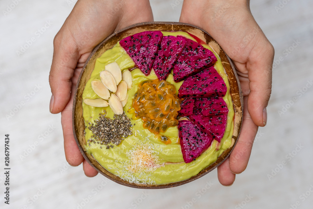 Green avocado smoothie in coconut bowl with dragon fruit, passion fruit, almond flakes, coconut chips and chia seeds for breakfast , close up. The concept of healthy eating, superfood Green avocado smoothie in coconut bowl with dragon fruit, passion fruit, almond flakes, coconut chips and chia seeds for breakfast , close up. The concept of healthy eating, superfood