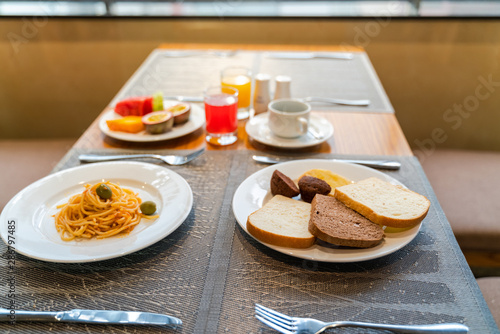 Fresh romantic breakfast table next to morning briliant light window  with bread  pastry  spaghetti  fruit  juice