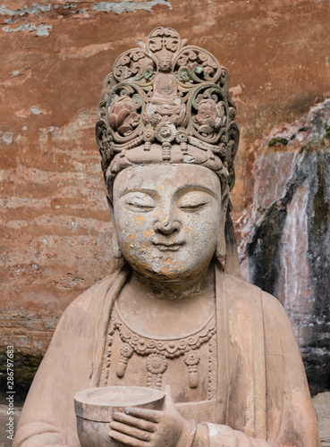 Statue of disciple or follower holding a bowl with two hands in front of giant Buddha at Dazu Rock Carvings at Mount Baoding or Baodingshan in Dazu, Chongqing, China. UNESCO World Heritage Site. 