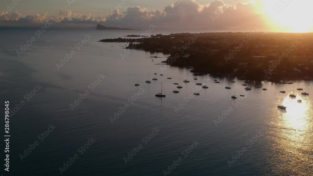 Aerial shot above sport boats anchored near the coast. The shot it´s taken by the dawn, with the sun rising at the right. At the background, over the horizon, you can see Flat island, Mauritius Aerial shot above sport boats anchored near the coast. The shot it´s taken by the dawn, with the sun rising at the right. At the background, over the horizon, you can see Flat island, Mauritius