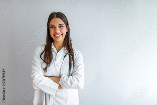 Portrait of an attractive young female caucasian doctor in white coat. Smiling female medical doctor, healthcare professional with labcoat and stethoscope. Isolated on grey background. photo