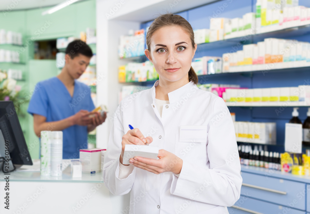 Female pharmacist is attentively stocktaking medicine with notebook