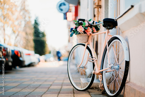 White bicycle with basket of flowers standing near the door on the street in city.