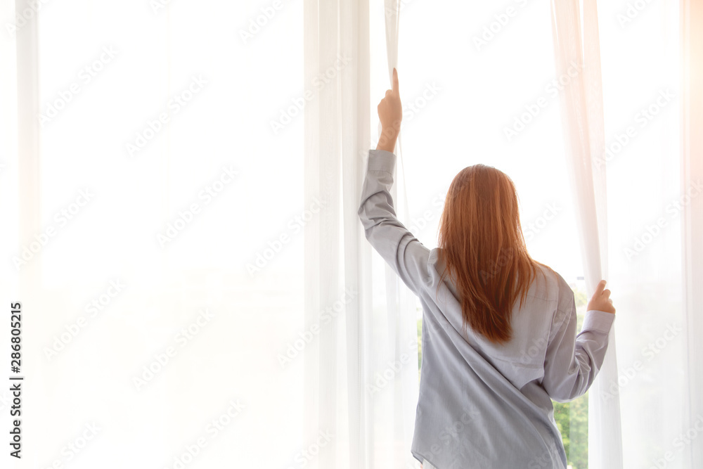 Close up of happy young woman opening window curtains at home. Concept of people ready to start day with fresh life and ready for work. Free copy space.