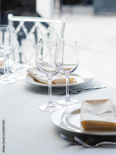 Table served for banquet with cutlery, wine glasses and napkins. Pastel colored decorations.