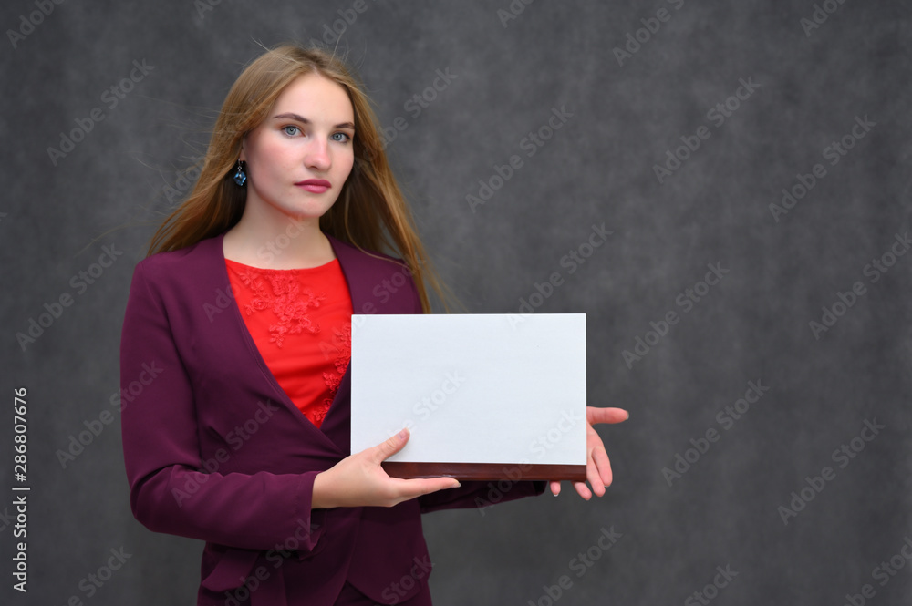 Portrait of a pretty secretary manager brunette girl with long flying hair in a burgundy business suit with a folder on a gray background. Smiling, showing emotions. Portrait of a pretty secretary manager brunette girl with long flying hair in a burgundy business suit with a folder on a gray background. Smiling, showing emotions.