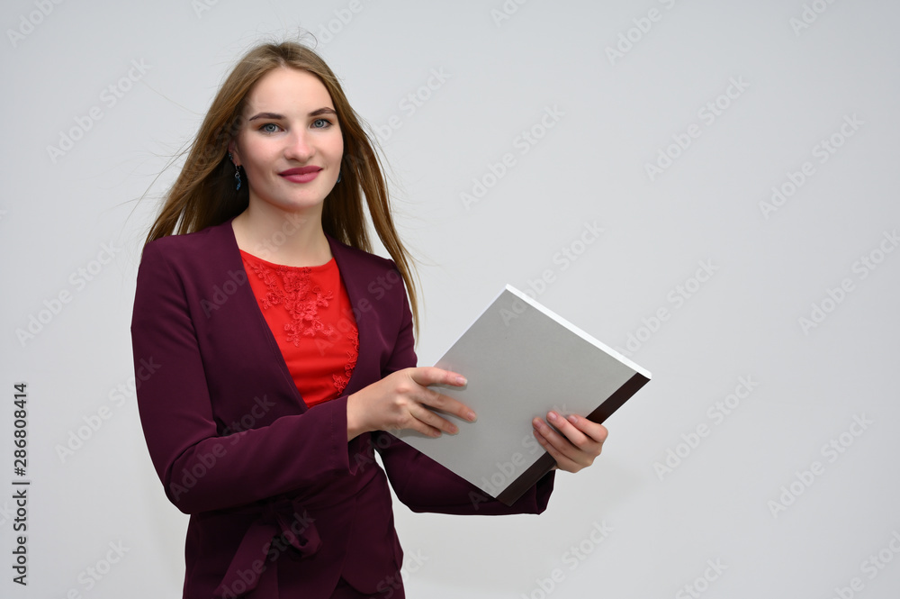 Portrait of a pretty secretary manager brunette girl with long flying hair in a burgundy business suit with a folder on a white background. Smiling, showing emotions. Portrait of a pretty secretary manager brunette girl with long flying hair in a burgundy business suit with a folder on a white background. Smiling, showing emotions.