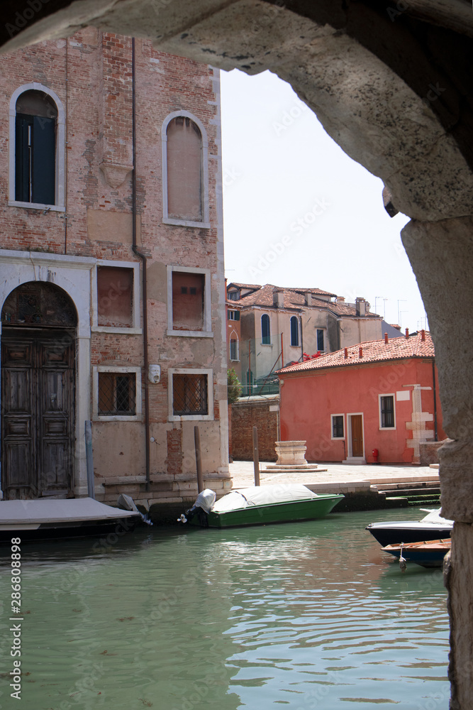 View of the Venetian canal, old building and the street through the arch