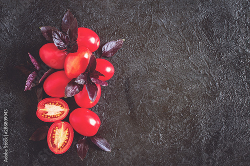 red fresh tomatoes and purple Basil leaves on a dark background. background with tomatoes top view. copy space. flat lay.