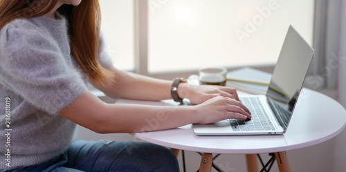Close-up view of young female freelancer working on her project while typing on laptop