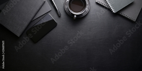 Dark trendy workplace with smartphone and office supplies on black leather table background