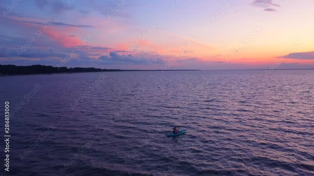 A dramatic drone shot of a lone kayaker slowly driffting into a colorful sunset A dramatic drone shot of a lone kayaker slowly driffting into a colorful sunset