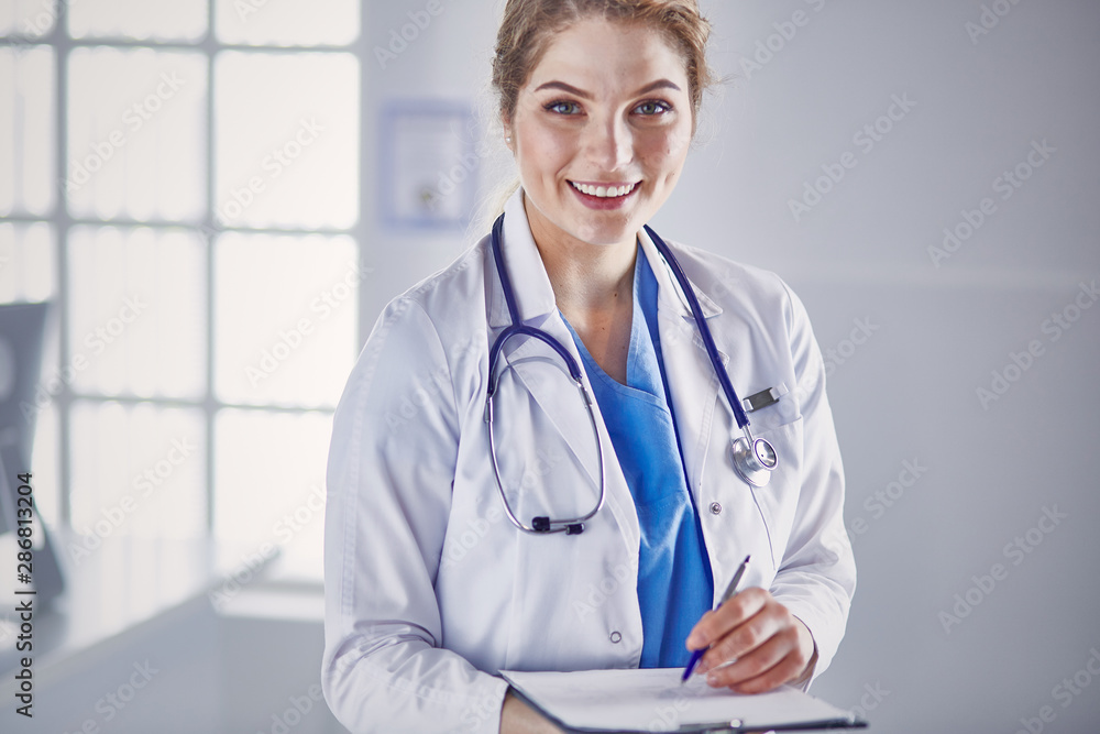 Young woman doctor is standing with board with clipboard smilin Young woman doctor is standing with board with clipboard smilin