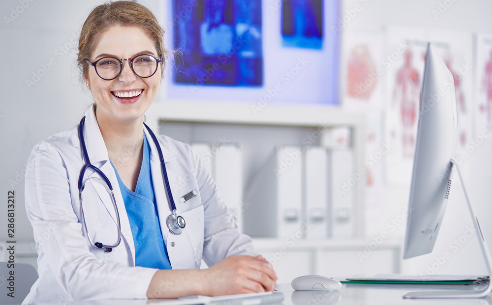 Beautiful young smiling female doctor sitting at the desk Beautiful young smiling female doctor sitting at the desk