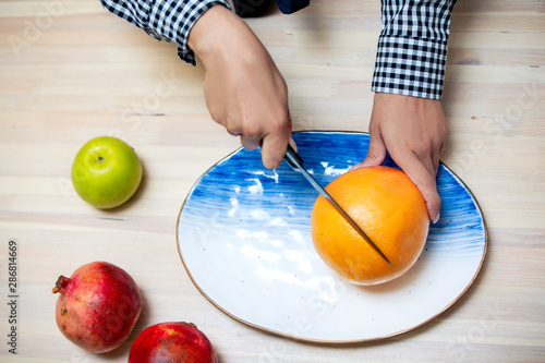  Girl cuts grapefruit on a beautiful blue and white plate on a wooden table