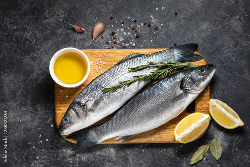 Fresh fish seabass and ingredients for cooking, lemon and rosemary. Dark background top view. photo