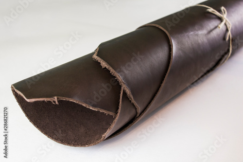 roll of dark brown leather tied with a beech rope close up on a white background