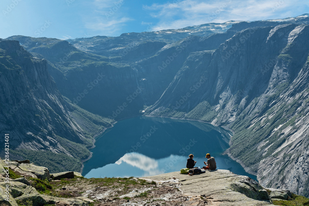 Couple sitting on the shore of mountain lake, Norway. Ringedalsvatnet lake landscape, way to Trolltunga rock.