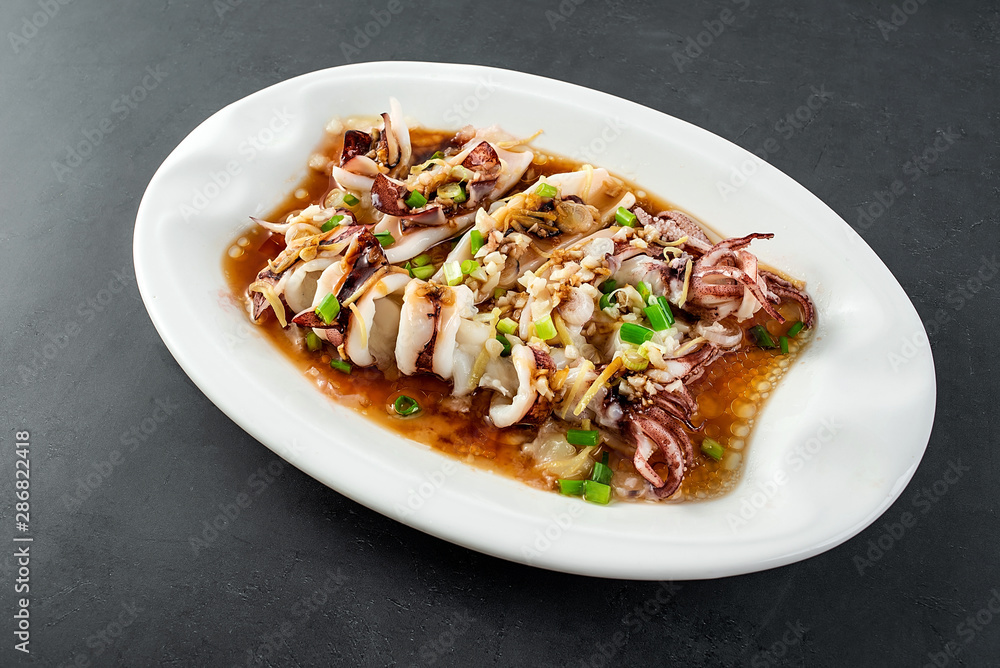 Chinese Chaoshan home cooking, a plate of oyster sauce steamed small squid on a black background Chinese Chaoshan home cooking, a plate of oyster sauce steamed small squid on a black background